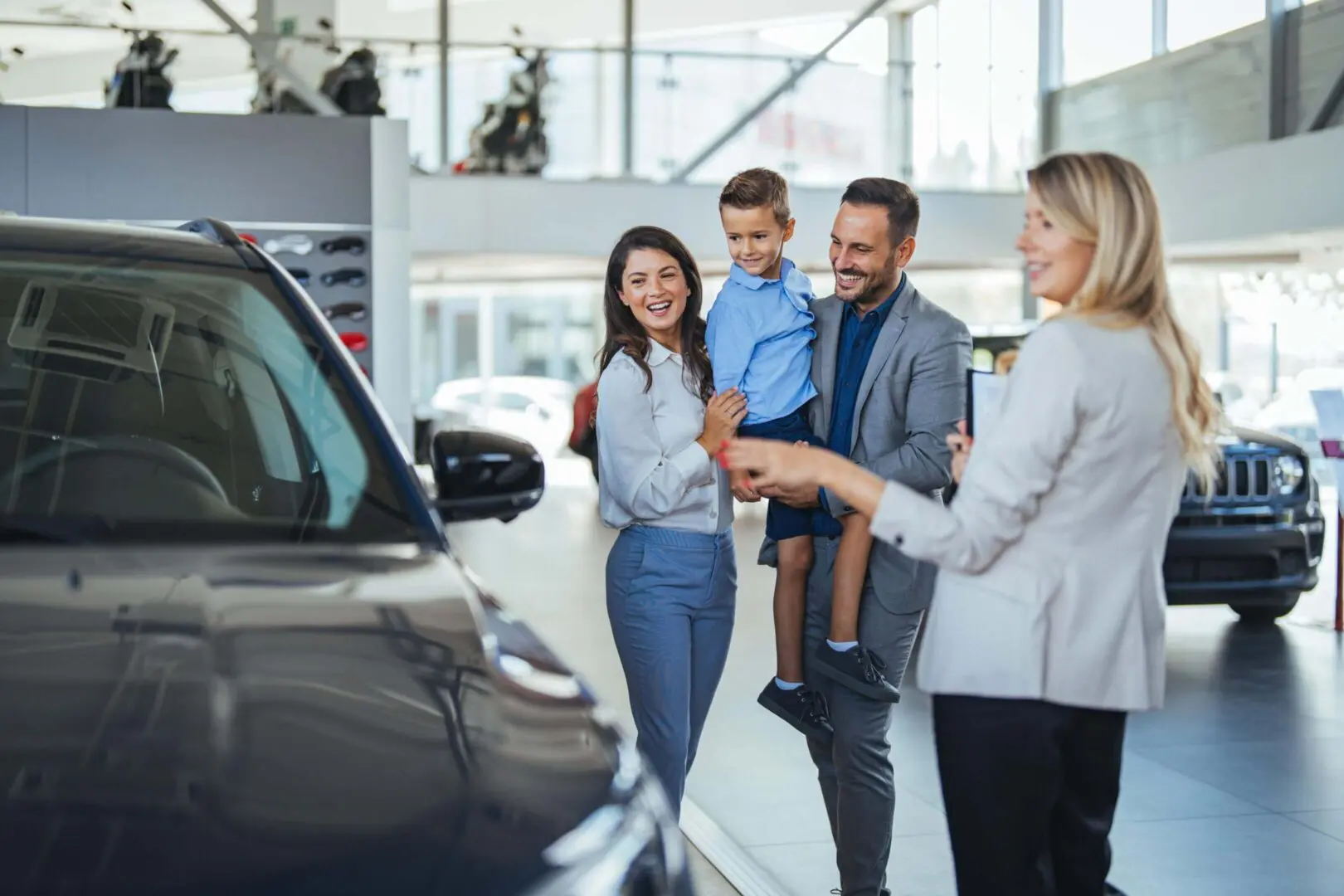 We offer cleaning & porter services for car dealers. Image of a family exploring cars at a dealership showroom.